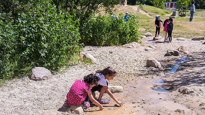 Kinder spielen am Wasserlauf des neuen Naturerfahrungsraum Tempelschlucht auf dem Tempelhofer Feld